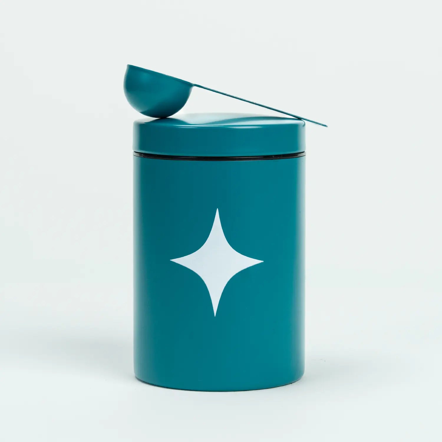 Magic Scoop turquoise metal container for daily greens powder, featuring a white sparkle logo and matching measuring scoop on the lid, ideal for storing all-in-one nutritional supplements
