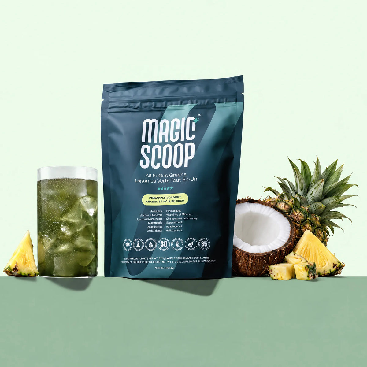 All-In-One Greens Pouch in Pineapple Coconut next to an iced glass of greens, a halved coconut and fresh pineapple.