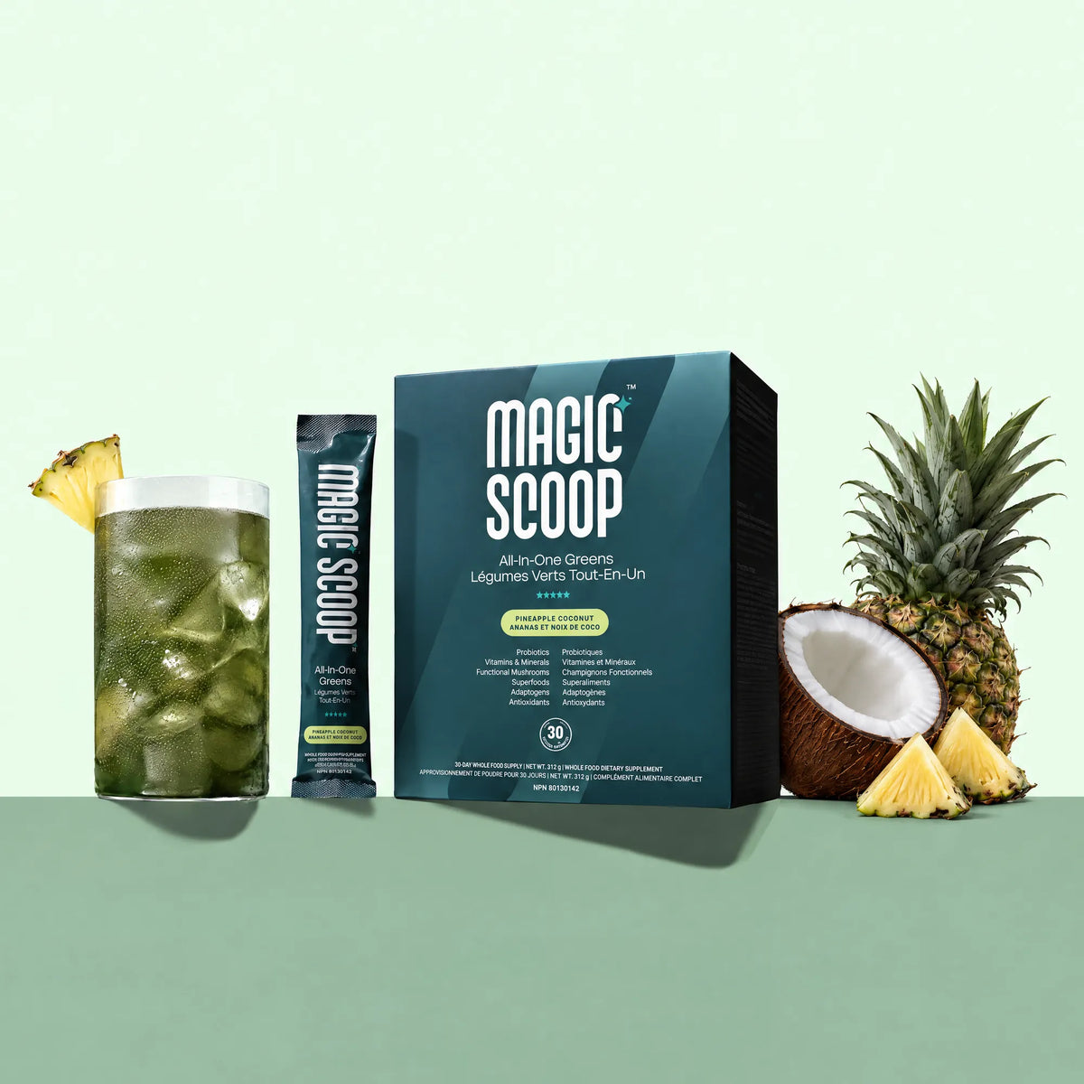 All-In-One Greens 30-Day Stick Packs box and single stick in Pineapple Coconut next to an iced glass of greens with a pineapple wedge, a halved coconut and a whole pineapple.