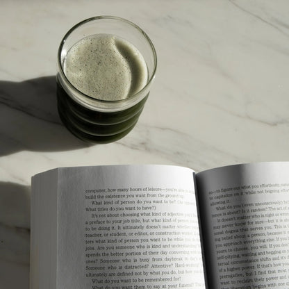 Short glass of Magic Scoop next to an open book on a light surface.