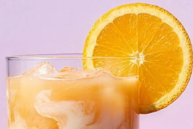 A tall glass of creamy orange Magic Scoop Electrolytes + Creatine over ice with an orange wheel.