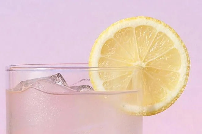 A tall glass of pink lemonade Magic Scoop Electrolytes + Creatine over ice with a lemon wheel.