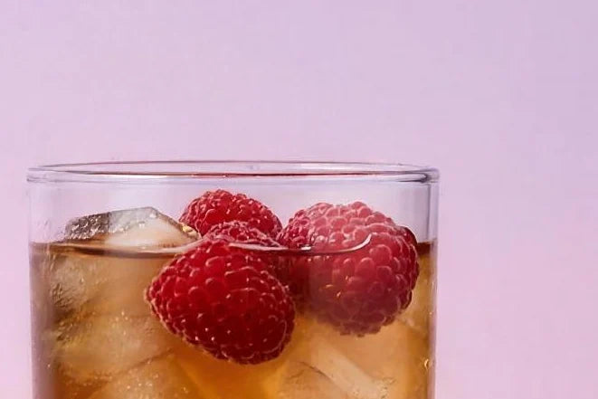A tall glass of raspberry iced tea Magic Scoop Electrolytes + Creatine over ice with fresh raspberries.